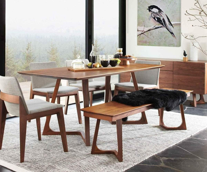 A modern dining room with a wooden table, four Fuchsia Dining Chairs, and a bench with a black throw. A large window shows trees outside. Sleek modern Fuchsia Dining Chairs surround the table, complementing the clean lines of the space. A bird painting hangs on the wall above a wooden sideboard.