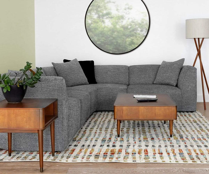 A modern living room featuring a gray sectional sofa, wooden coffee and side tables, a potted plant, and the Gaffel Floor Lamp with its distinctive tripod base. A round mirror on the wall and a patterned rug on the floor complete this inviting home decor.