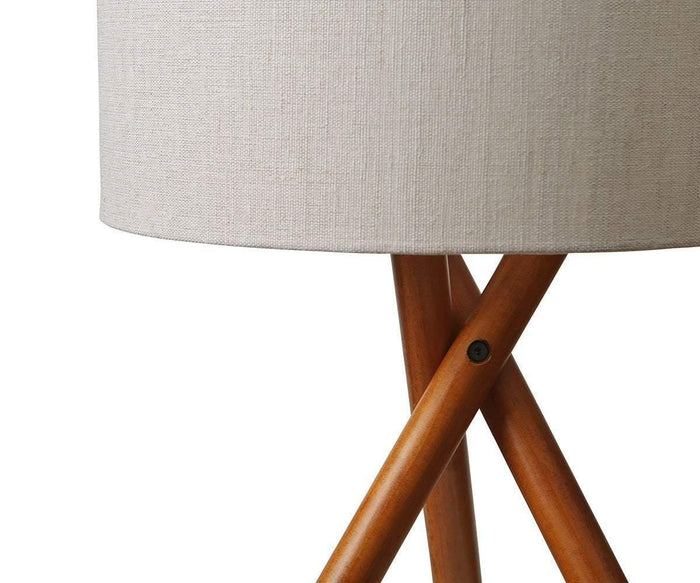 A close-up of the Gaffel Table Lamp featuring a beige fabric shade and a wooden tripod base that crosses elegantly at the center, set against a white background—making it an ideal choice to enhance your home decor.