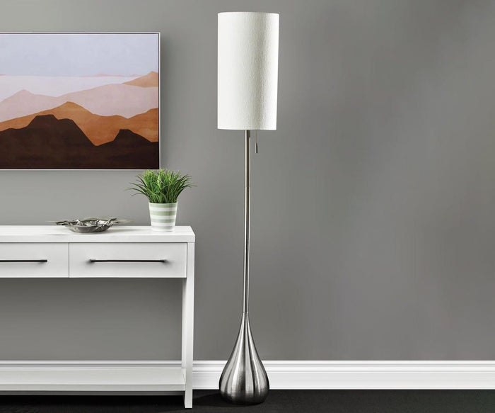 A modern living room with a white console table, potted plant, mountain wall art, and the Gemma Floor Lamp—featuring a brushed steel base and a white fabric shade—against a gray wall.