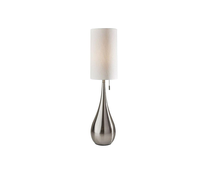 The Gemma Table Lamp, in brushed steel, showcases a metallic teardrop-shaped base paired with a tall cylindrical white lampshade for a look of contemporary glamor. It is photographed against a plain white background.