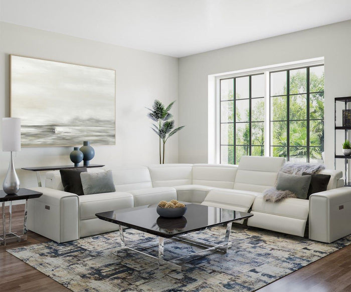 Modern living room featuring a white sectional sofa, glass coffee table, abstract wall art, and two side tables each topped with the Gemma Table Lamp—a stylish lighting piece with a brushed steel base. A potted plant and large windows overlooking greenery bring freshness indoors, while a geometric-patterned rug on wooden floors completes the contemporary glamour of the space.
