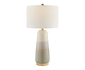 The Ghazi Table Lamp features a modern, minimalist design with a cylindrical white linen shade and a ceramic base in gradient shades of beige and gray, all resting on a wooden platform. The lamp comes in Grey/Multi.