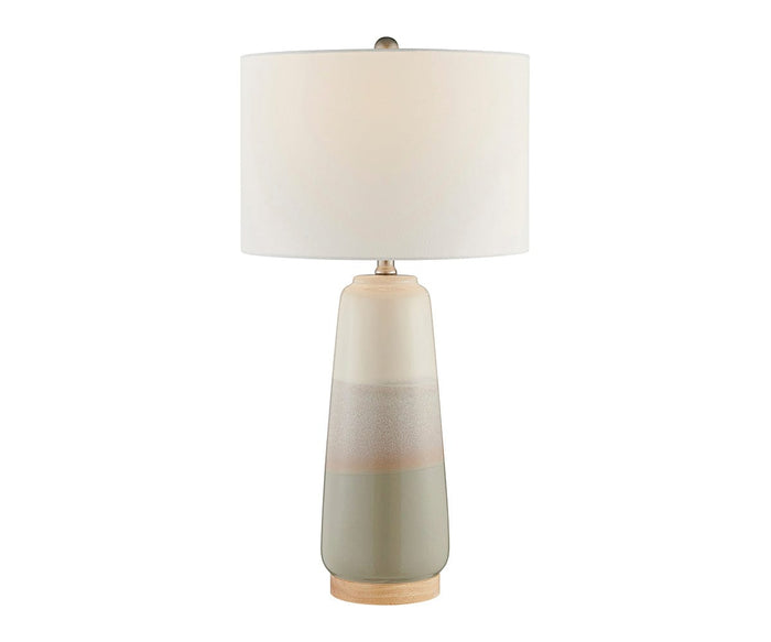 The Ghazi Table Lamp features a modern, minimalist design with a cylindrical white linen shade and a ceramic base in gradient shades of beige and gray, all resting on a wooden platform. The lamp comes in Grey/Multi.