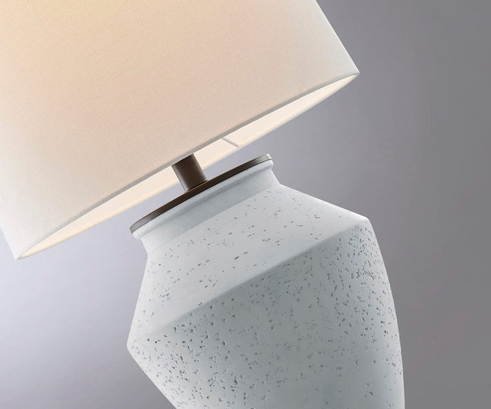 A close-up of the Glenn Table Lamp reveals its textured white ceramic base and light beige lampshade, set against a soft gray background—an elegant indoor-outdoor lamp designed to complement any space.