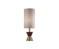The Grazia Table Lamp, featuring a tall, cylindrical beige fabric shade and an hourglass-shaped brass base accented with walnut wood at the center, is displayed against a plain white background.