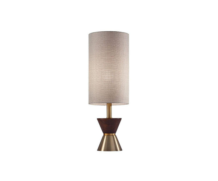 The Grazia Table Lamp, featuring a tall, cylindrical beige fabric shade and an hourglass-shaped brass base accented with walnut wood at the center, is displayed against a plain white background.