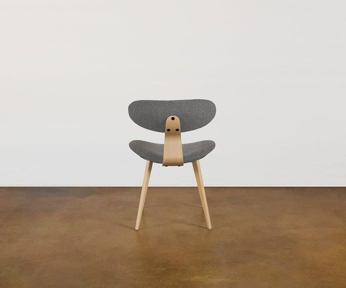 The Hana Dining Chair, featuring solid white oak legs and frame with a gray upholstered seat and backrest in performance fabric, sits on a brown floor against a plain white wall.