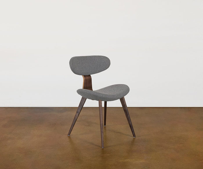 The Hana Dining Chair, featuring a modern Scandinavian design with a curved gray performance fabric seat and backrest, supported by three angled walnut legs, is placed on a brown polished floor against a plain white wall.