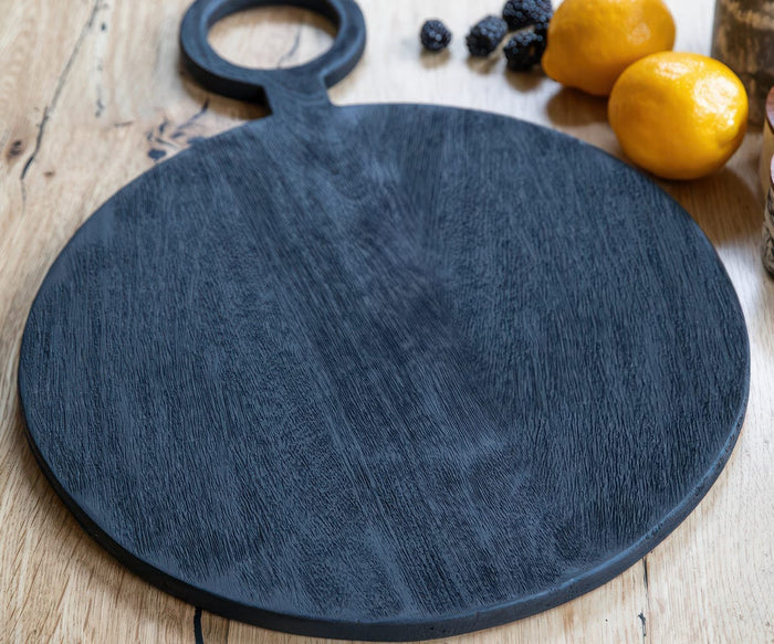 A handcrafted Hava Round Board in black sits on a light wooden surface. Two lemons and a few blackberries are placed nearby, highlighting the sustainable serving board’s elegant design and functionality.