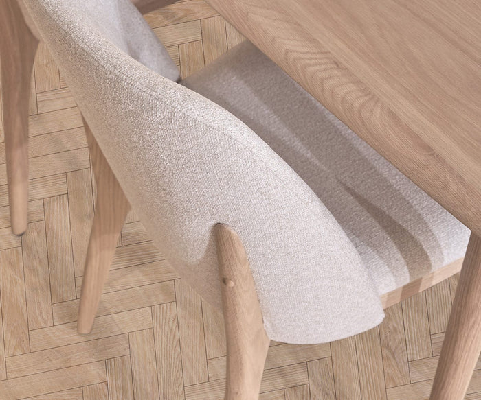A light wood dining table and a Hendrick Dining Chair – White Oak, featuring a cushioned seat with beige upholstery, are set on a light wood herringbone-pattern floor, viewed from above.