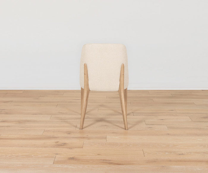 A Hendrick Dining Chair - White Oak, featuring a cream-colored cushioned seat and light white oak frame, is shown from the back sitting on a light wood floor against a plain white wall.