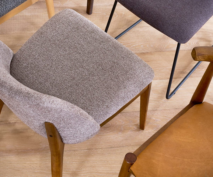 Four Hendrick Dining Chairs, each showcasing unique upholstery and leg designs, are grouped closely together on a light wooden floor as seen from above. Every Hendrick Dining Chair features a cushioned seat and sturdy frame, blending comfort with enduring style.