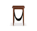 The Hendrick End Table with Hanging Shelf, shown in Timber Brown against a white background, is a small mid-century piece crafted from American poplar wood. It features four legs with elegant brass caps, a flat rectangular top, and a black leather sling hanging underneath for storage.