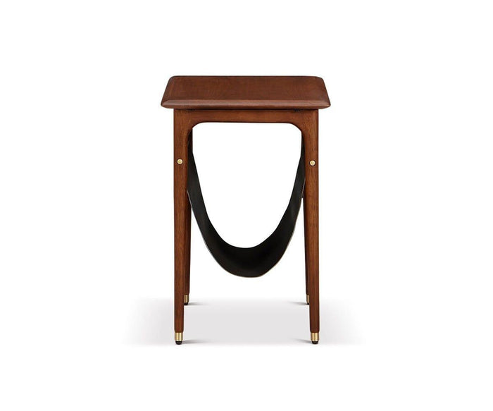 The Hendrick End Table with Hanging Shelf, shown in Timber Brown against a white background, is a small mid-century piece crafted from American poplar wood. It features four legs with elegant brass caps, a flat rectangular top, and a black leather sling hanging underneath for storage.