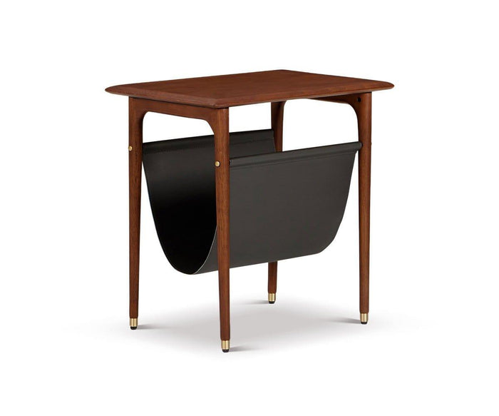 The Hendrick End Table with Hanging Shelf, crafted from American poplar wood, features elegant tapered legs with brass caps and a black leather sling below for magazine storage, shown against a white background.