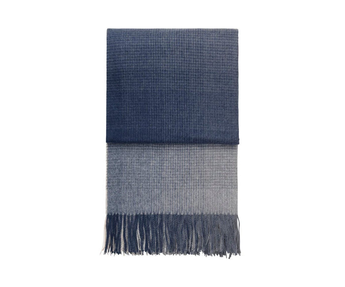 Introducing the Horizon Throw, an eco-friendly accent crafted from recycled alpaca wool. This folded throw features a checkered pattern in dark blue on the upper section and light gray on the lower section, complete with fringed ends for added texture.