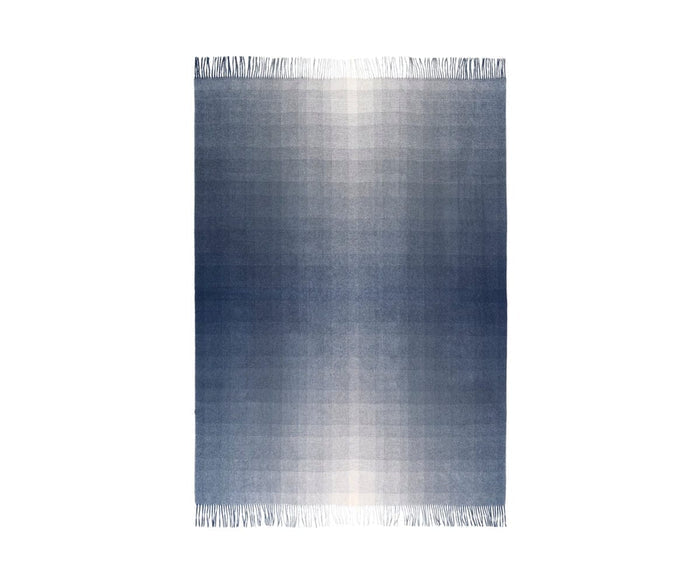 The Horizon Throw is a rectangular fringed rug featuring a gradient pattern that transitions from deep blue at the edges to soft blue and white at the center, displayed against a white background. Designed for sustainable home decor, it is thoughtfully crafted from recycled alpaca wool.