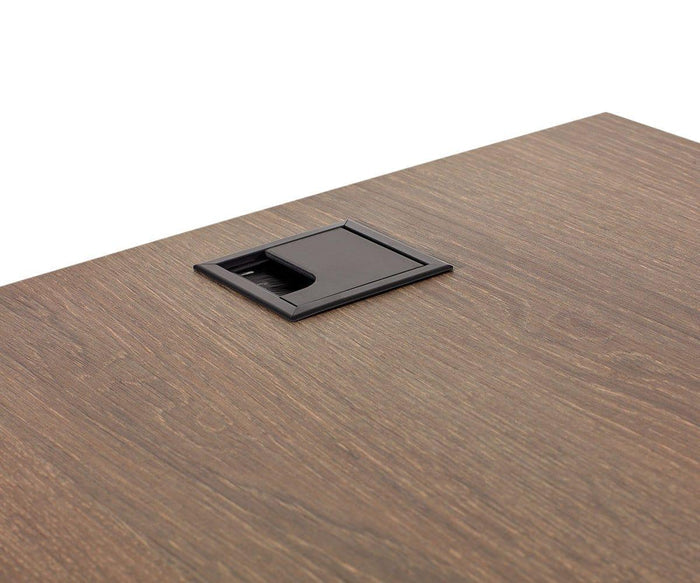 A close-up of a wooden desk featuring a rectangular black cable management grommet embedded near the edge of the surface, highlighting the sophisticated design characteristic of modern office furniture such as the Inari 47″ Desk.