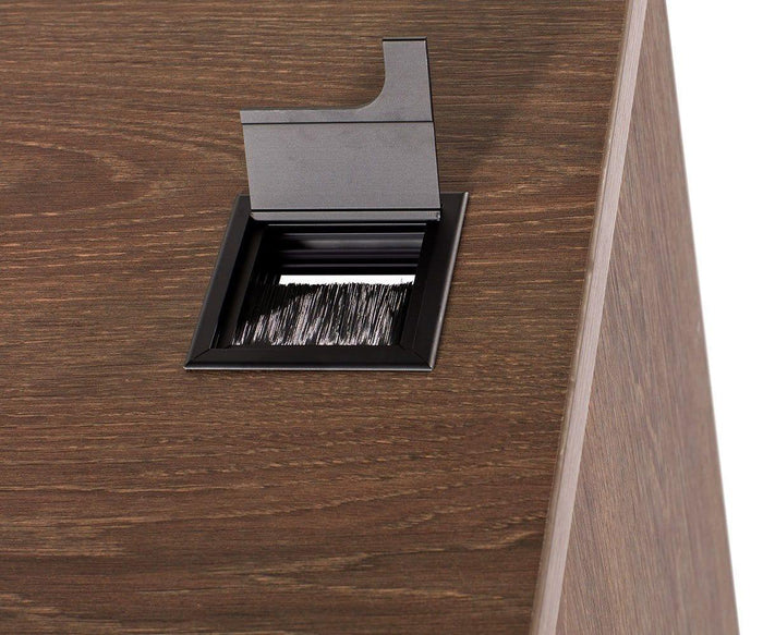 A close-up of a rectangular cable management grommet with a brush insert on a wooden desk surface, allowing cables to pass through while keeping dust out—a sleek solution featured in modern desk designs such as the Inari 47″ Desk and other contemporary office furniture.