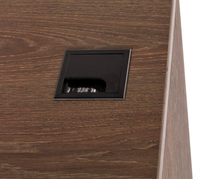 A close-up of a wooden modern desk, the Inari 47″ Desk, showcases a square black cable grommet with a small brush opening for organizing and routing cables.
