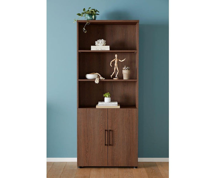 The Inari High Bookcase + Door Set features two cabinet doors at the bottom and three open, adjustable shelves styled with plants, books, decorative objects, and a wooden mannequin—ideal for adding stylish storage to your office. Shown here against a blue wall on a wooden floor.