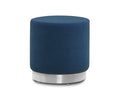 The Isla Ottoman, featuring a round silhouette and smooth blue velvet upholstery, is displayed against a white background.
