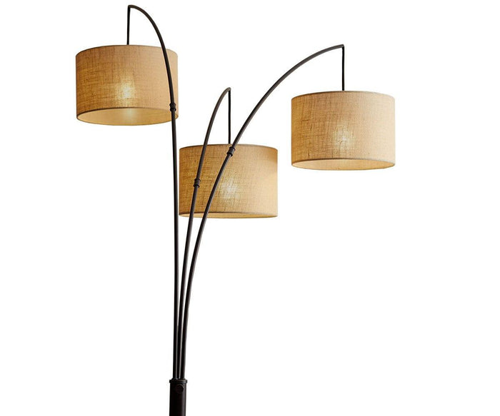 The Jan 3-Light Arch Floor Lamp features three gracefully curved metal arms, each supporting a cylindrical beige textured fabric shade, creating a softly illuminated ambiance.