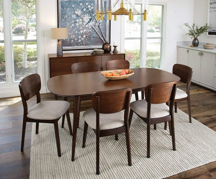 A modern dining room with a walnut veneer wooden table, six Juneau Dining Chairs featuring cream fabric seats, a bowl of fruit, light rug, console with lamp, and large framed art. Sunlight streams in through tall windows.