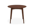 The Juneau Round Table, finished in walnut, features a round wooden top and four slightly angled, tapered legs, showcasing a mid-century modern and Scandinavian design. It is presented against a white background.