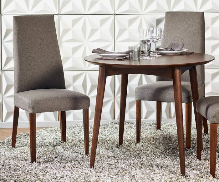 A Juneau Round Table with elegant tapered legs exemplifies Scandinavian design, paired with three upholstered chairs on a shaggy rug. The table is set with plates, utensils, glasses, and napkins, while the background features a geometric white wall pattern.