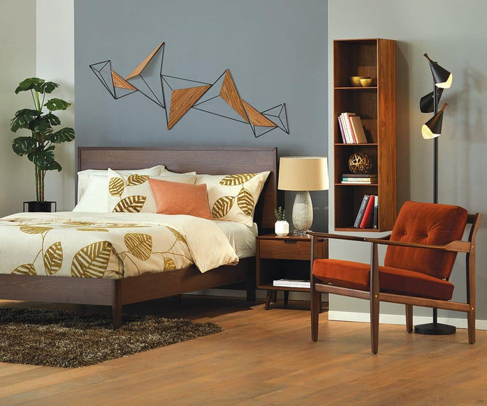 A mid-century modern bedroom featuring a wooden bed, leaf-patterned bedding, and an orange accent chair is complemented by a bookshelf and the Kabrino Floor Lamp with adjustable shades. The space is finished with a potted plant, abstract wall art, and light wood flooring.