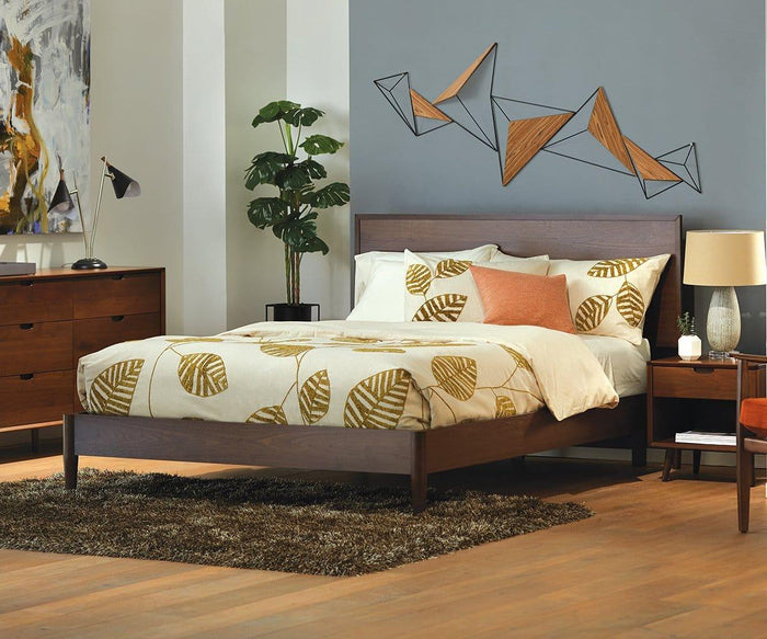 A modern bedroom with a wooden bed, leaf-patterned bedding, geometric wall art, a dresser, nightstands, the Kabrino Table Lamp with adjustable shades, a plant, and a brown rug on a wooden floor.
