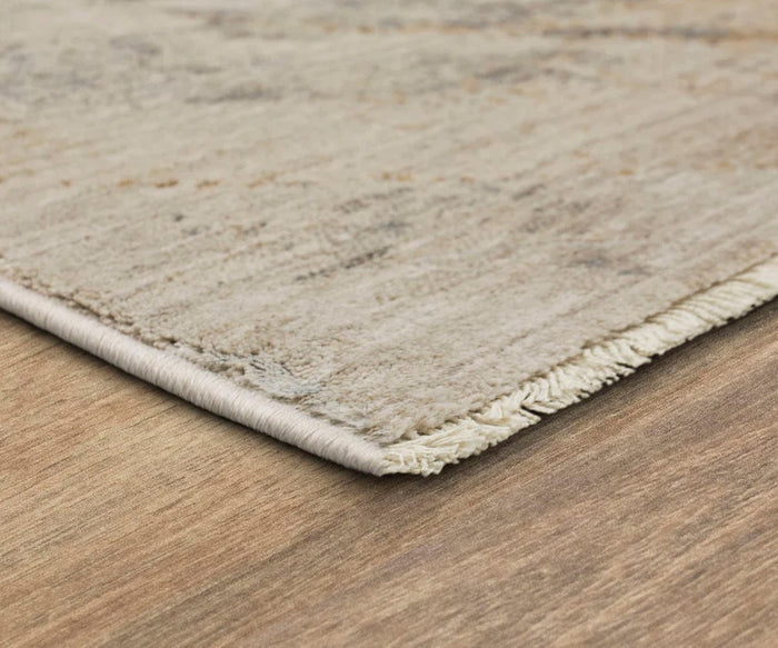 A close-up of the corner of the Karastan Echo Tesoro Rug in Cream, featuring a textured, durable design with fringe, placed on a wooden floor.