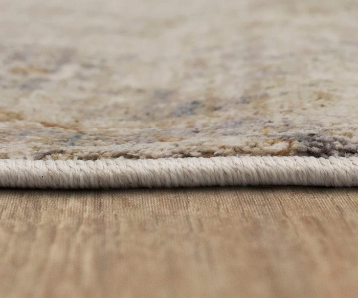 Close-up side view of the thin, light-colored Karastan Echo Tesoro Rug in Cream, featuring a textured surface and lying flat on a wooden floor. The edge of this durable area rug is neatly finished with tightly wrapped fibers.
