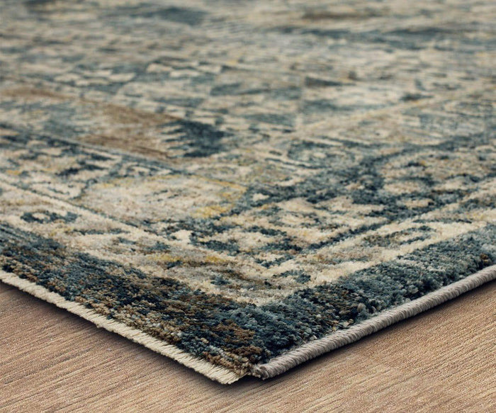 Close-up of the Karastan Marash Karamar Rug - Blue, featuring a blue and beige pattern with detailed texture and edging on a wooden floor.