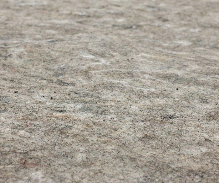 Close-up view of the Karastan Rug Pad’s rough, textured gray surface with subtle color variations and scattered fibers, resembling felt or insulation material—ideal as a non-slip rug pad that provides both cushioning and reliable protection for your rug.