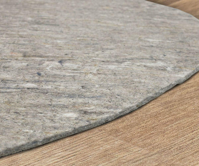 A close-up of the edge of a round, gray felt rug on a wooden floor highlights the texture and thickness of the rug material, with subtle emphasis on how adding a Karastan Rug Pad can provide extra protection and prevent slipping.