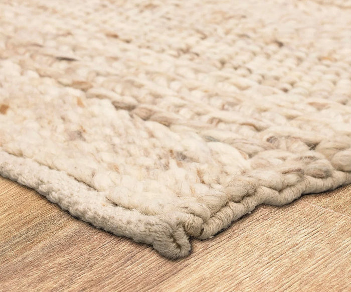 A close-up of the Karastan Tableau Roma Rug in Oyster, featuring its cream-colored, hand-loomed wool construction with thick, textured yarn on a light wooden floor. The image highlights the rug’s edge and the bold texture of its chunky weave, exemplifying modern style and inviting appeal.