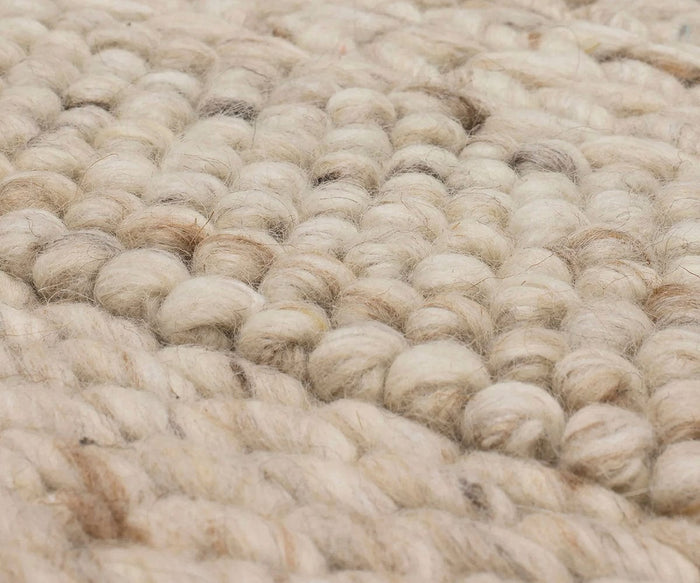 Close-up of the Karastan Tableau Roma Rug in Oyster, highlighting its thick, cream-colored and beige yarns woven into a chunky, textured pattern with visible fibers. This modern hand-loomed wool rug showcases the artistry of expert craftsmanship and contemporary design.