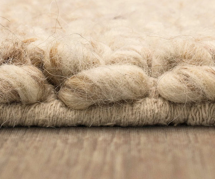 Close-up side view of the Karastan Tableau Roma Rug in Oyster, showcasing its textured, cream-colored hand-loomed wool with thick, knotted fibers resting on a wooden floor.