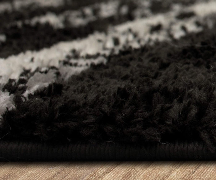 Close-up side view of the Karastan Traverse Lanes Rug in Charcoal, featuring a black and white textured design with thick fibers resting on a wooden floor. The image highlights the edge and pile height of this durable polyester rug, showcasing its suitability for high-traffic areas.