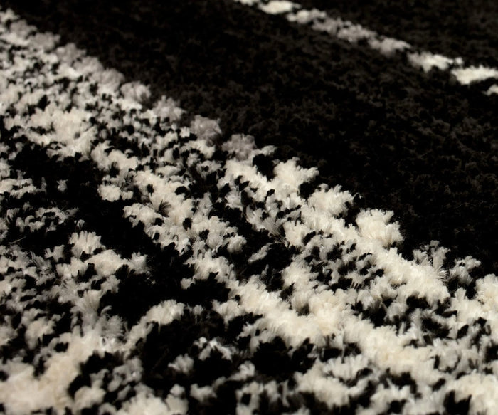 Close-up of the Karastan Traverse Lanes Rug - Charcoal, featuring a textured black and white pattern with soft, fluffy fibers and alternating dark and light stripes. Crafted from durable polyester, this modern rug is built to withstand daily wear in high-traffic areas while maintaining its inviting appearance.