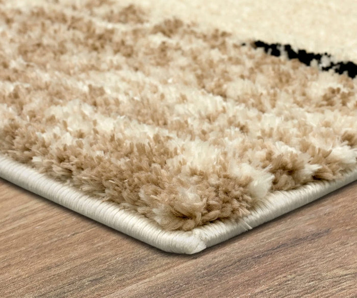 Close-up of the corner of a Karastan Traverse Lanes Rug - Tan on a wooden floor, highlighting the rug’s fluffy, durable polyester texture and neatly stitched edge.