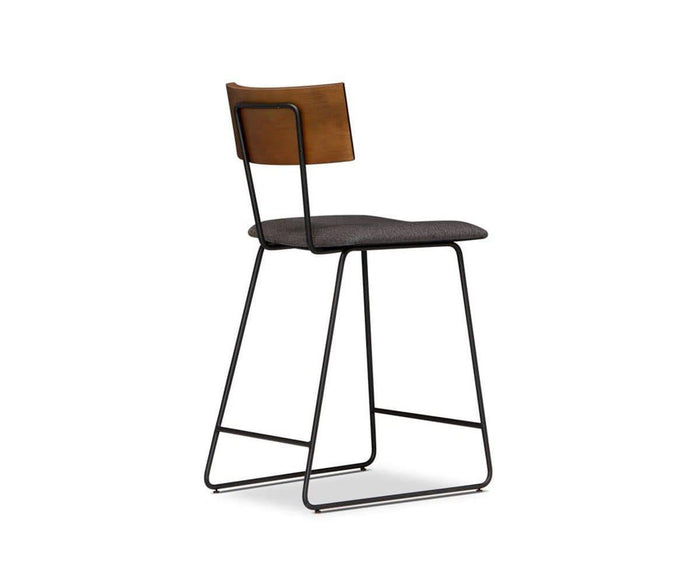 The Karsten Counter Stool with Back showcases a contemporary rustic industrial design, highlighted by its black metal frame, cushioned dark gray seat, and wooden backrest featuring subtle live edge detailing. It is presented at an angle against a white background.
