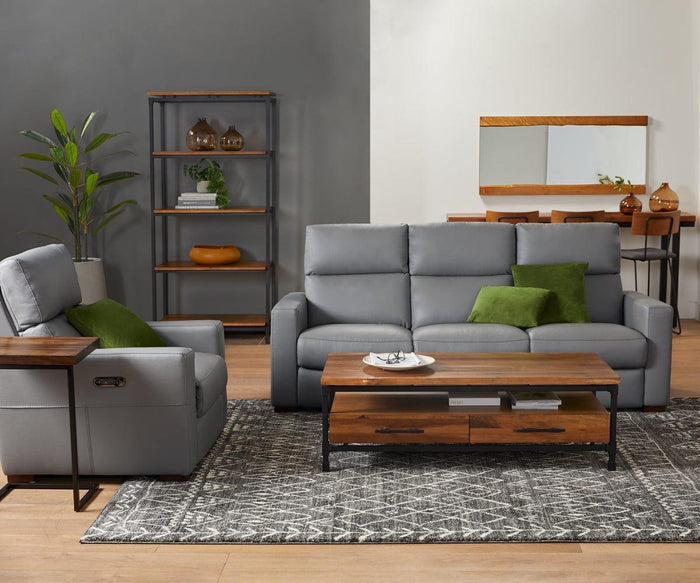 Modern living room with gray sofa and armchair, green accent pillows, wooden coffee table, geometric rug, open shelving, potted plant, and a dining area in the background featuring the Karsten Mirror crafted from solid American poplar wood.
