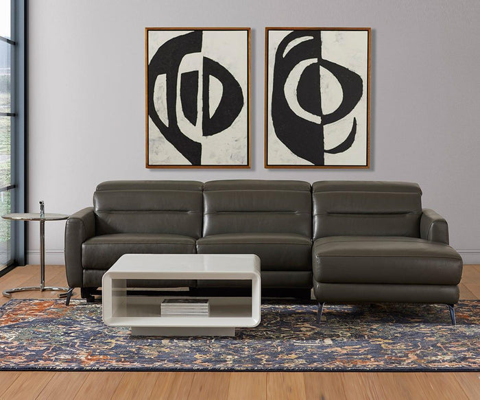 Contemporary living room furnished with a dark gray sectional sofa, abstract black and white wall art, a sleek white coffee table, and the Krom C-Table—an adjustable height modern side table—positioned next to the seating area. A patterned rug spans the wooden floor, with ample natural light streaming in from a large window on the left.