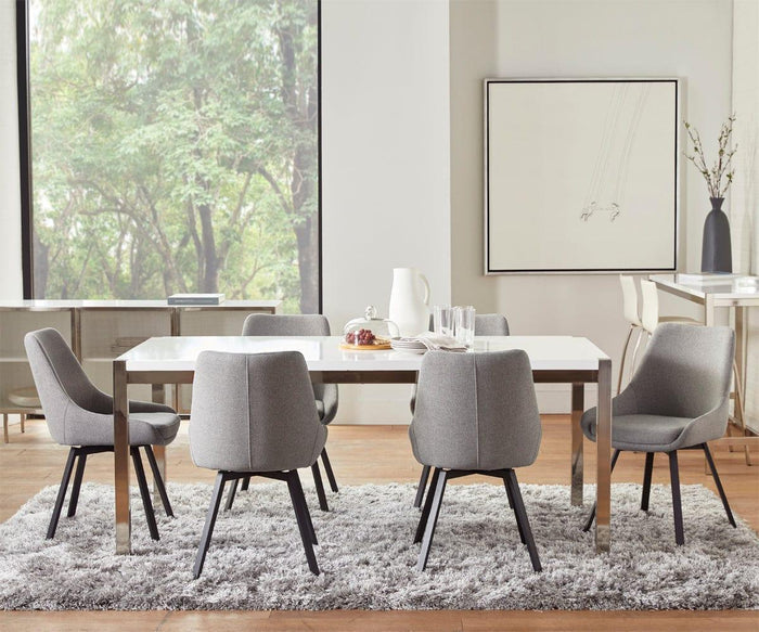 Modern dining room with a white table, six Kyla Swivel Dining Chairs featuring cushioned seats and sleek metal leg support, and a light gray rug. Large window with trees outside, minimalist artwork, and vases decorate the room.