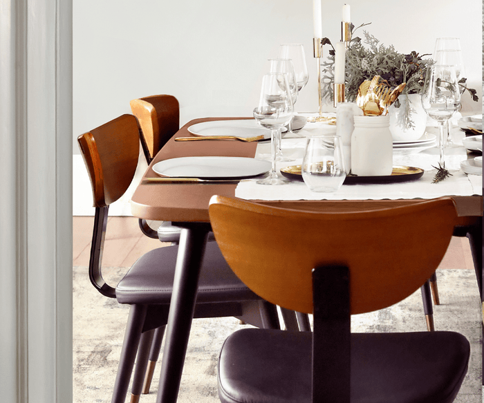 A contemporary mid-century Lanson Dining Table set for a meal with four wooden chairs in a rich walnut finish, white plates, wine glasses, candles, and a floral centerpiece atop a white table runner.