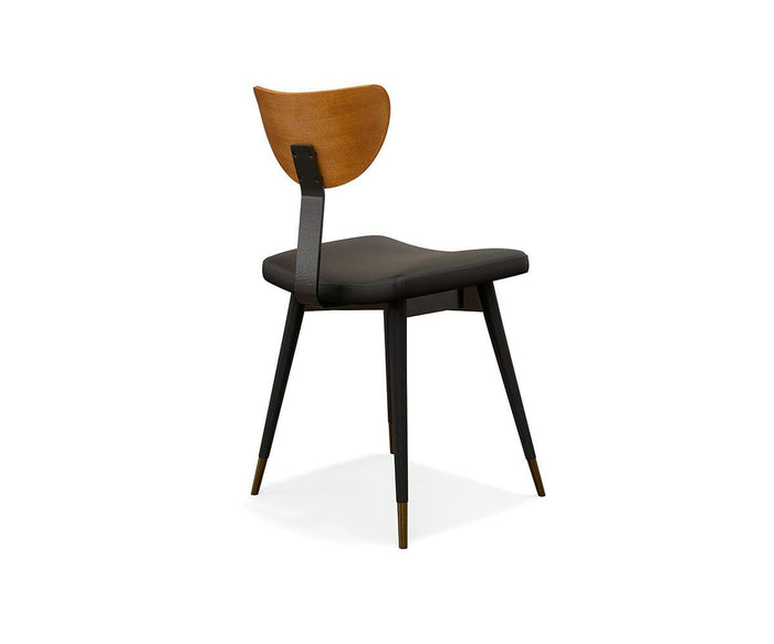 The Lanson Dining Chair showcases modern mid-century style with a seat cushioned in black faux leather, black tapered legs finished with brass tips, and a gracefully curved bentwood backrest, all presented at an angle against a white background.